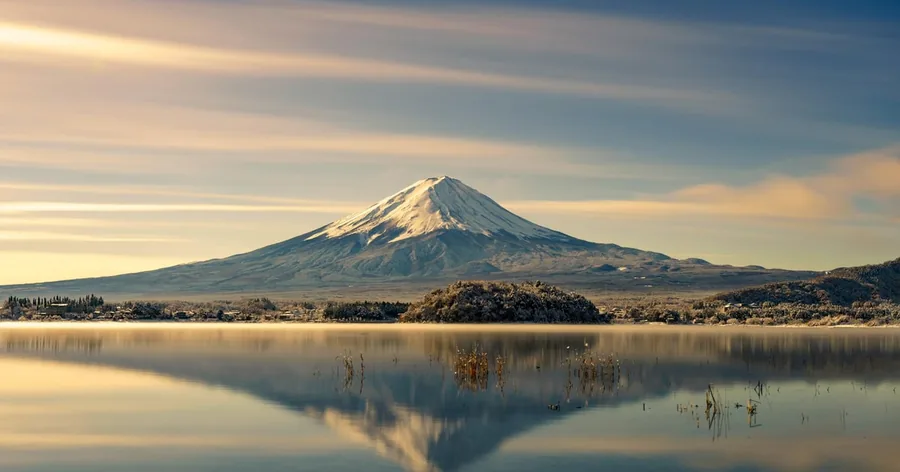 Der Fuji spiegelt sich in weichem goldenem Licht in einem stillen See
