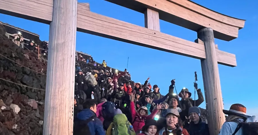Eine Menge Wanderer mit Stirnlampen unter einem hölzernen Torii auf dem Gipfel des Fuji in der Morgendämmerung